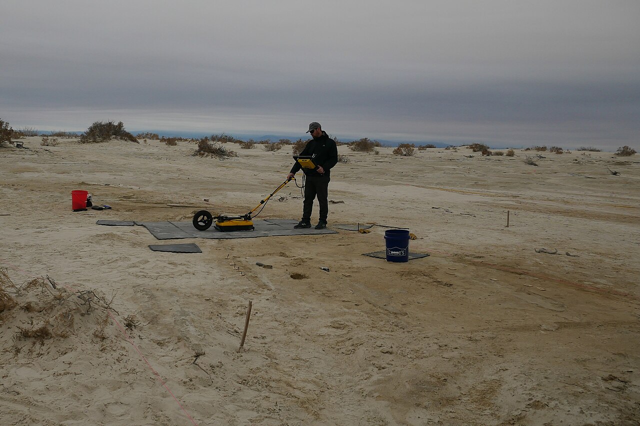 Researcher pulling a ground-penetrating radar unit across the ground during an archaeological survey